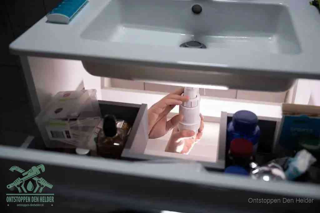 Een pompfles met zeep boven een wastafel, de heet water en afwasmiddel-methode om een vetprop in de afvoer los te maken in Den Helder