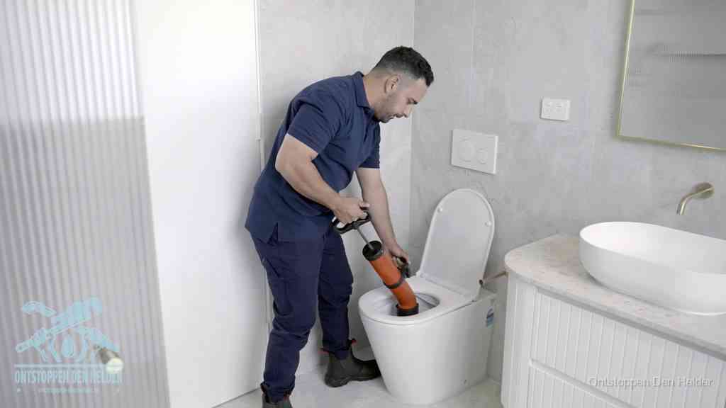 Een monteur buigt over een wandcloset en duwt met de hand een persluchtontstopper in de toiletpot om de verstopping handmatig los te maken in Den Helder