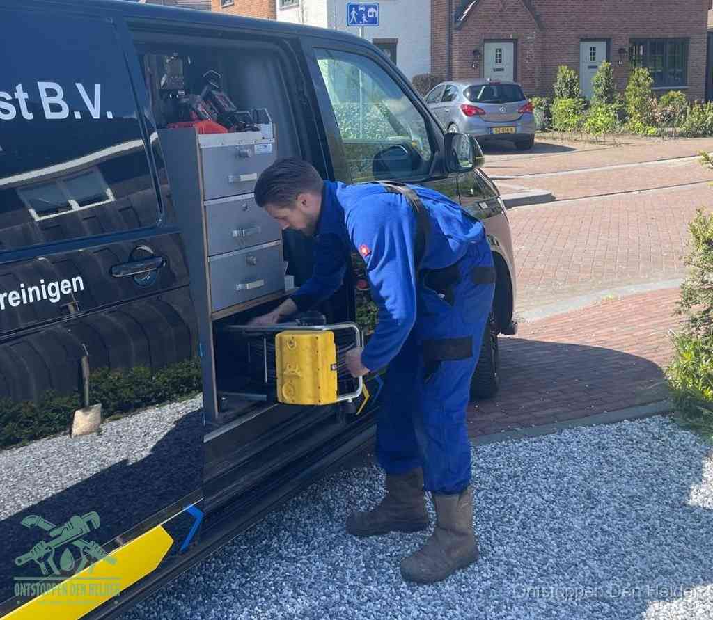 Een monteur pakt buiten op de oprit gereedschap uit de bedrijfsbus, het moment om een professional in te schakelen voor een verstopte afvoer in Den Helder