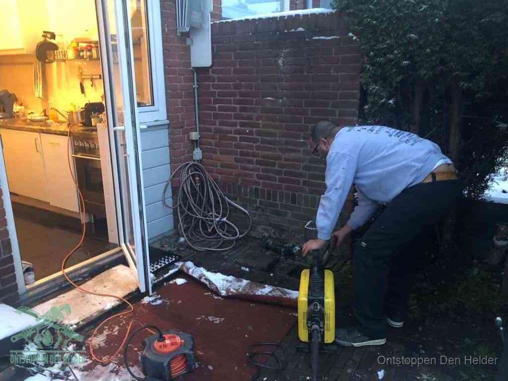 Een monteur werkt buiten bij een open riool-/grondput met een elektrische ontstoppingsmachine om een verborgen afvoerprobleem op te sporen in Den Helder