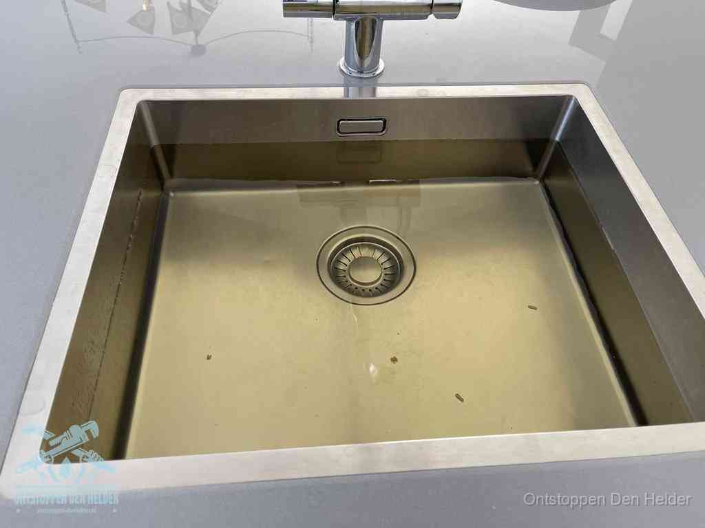 Stilstaand water in een rvs spoelbak dat niet wegloopt, een duidelijk signaal van een gootsteenverstopping in Den Helder