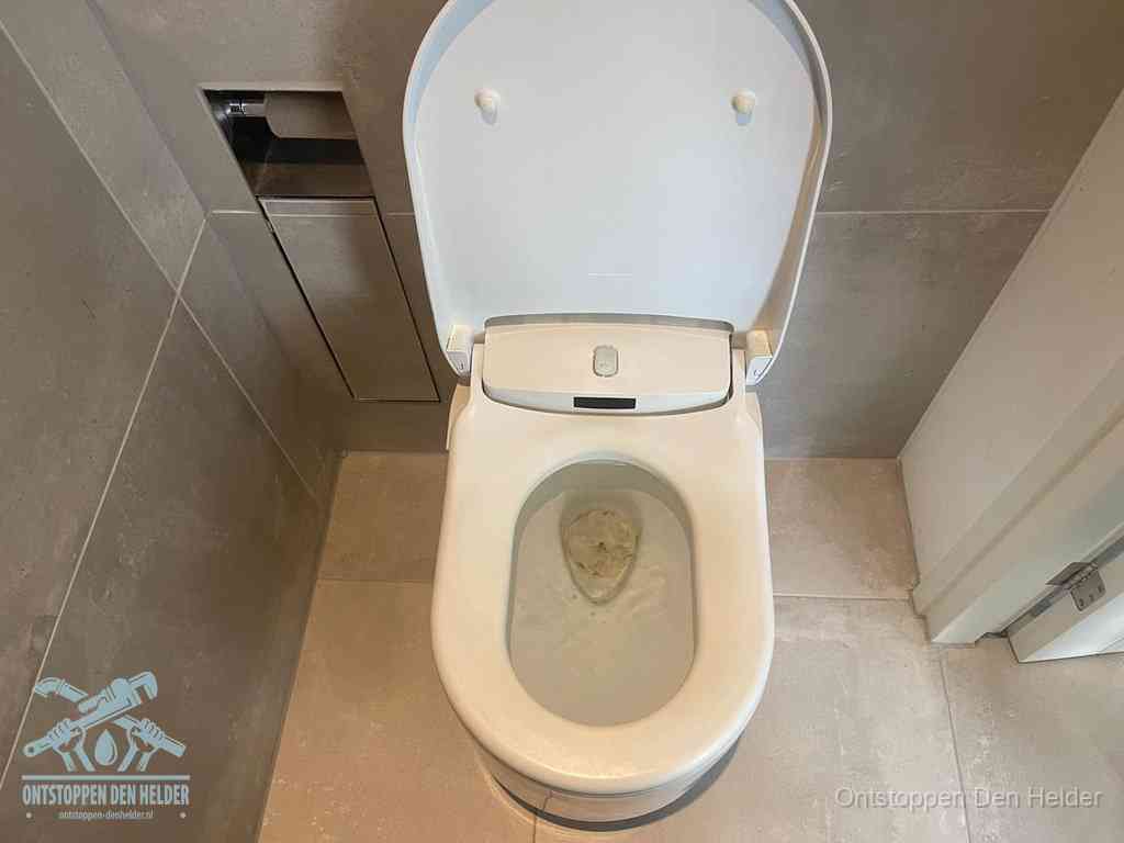 Een wit hangtoilet waarin een prop wc-papier op het water blijft drijven, een duidelijk signaal van een verstopte wc in Den Helder