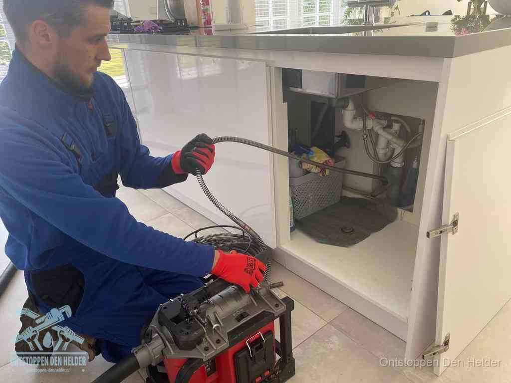 Een monteur reinigt de keukenafvoer grondig met een veermachine om terugkerende gootsteenverstoppingen te voorkomen in Den Helder