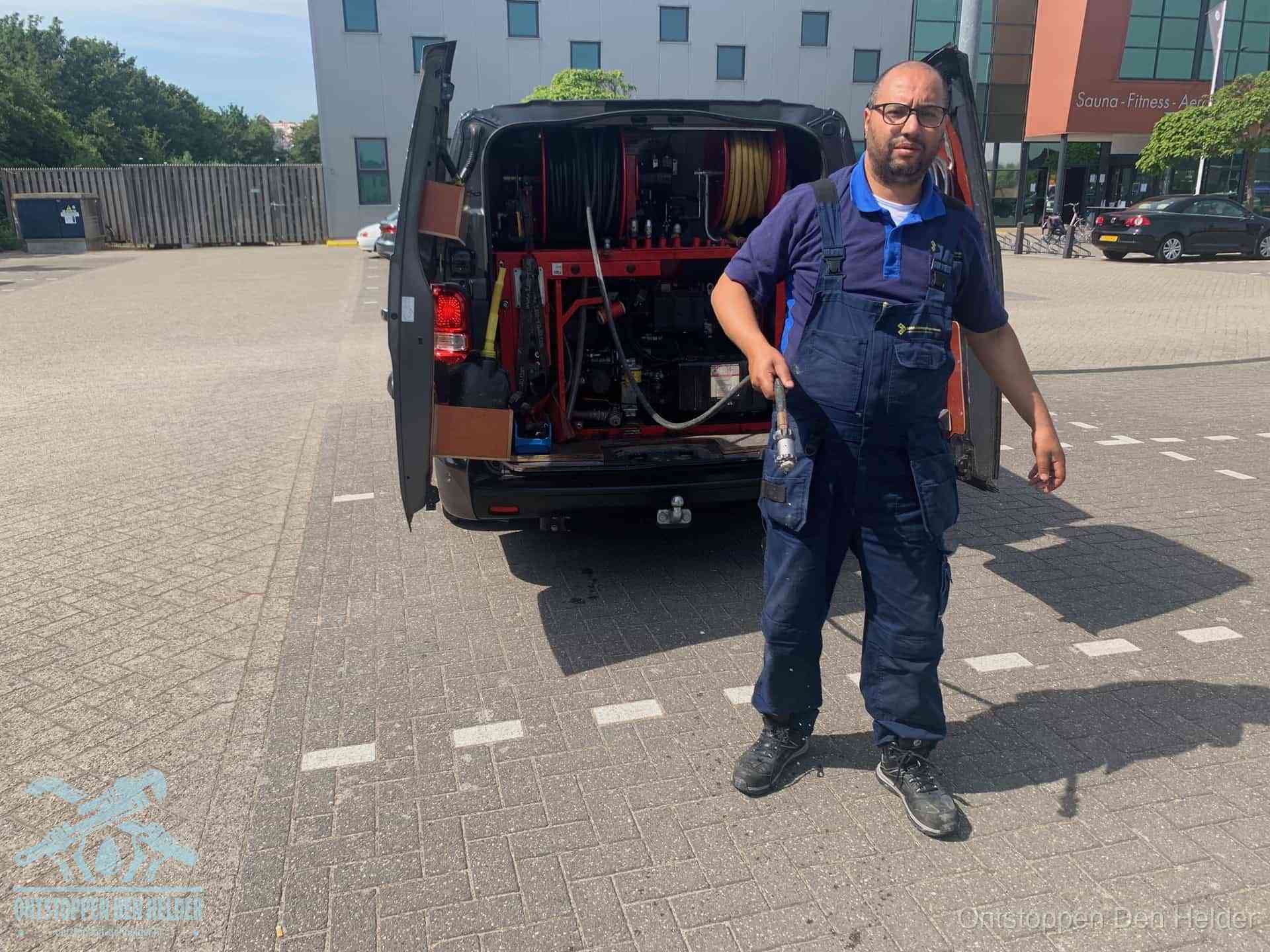 Een monteur bij zijn bestelbus met een hogedruk- en rioolreinigingsunit, klaar om de oorzaak van terugkerende wc-verstoppingen aan te pakken in Den Helder