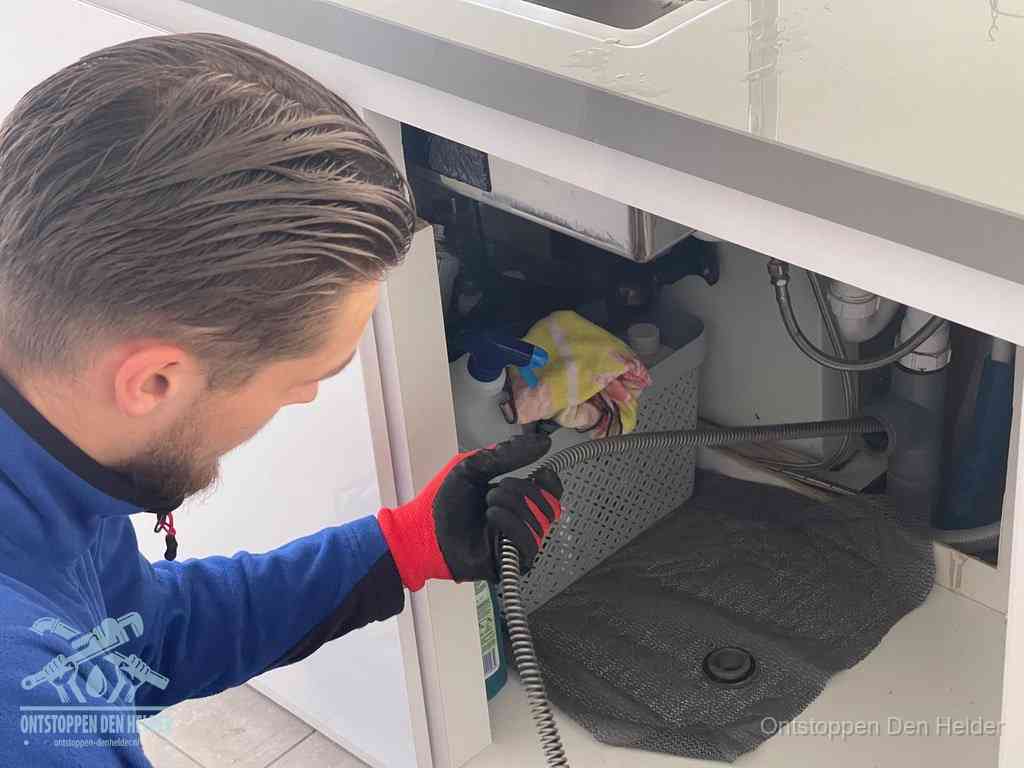 Een monteur voert een flexibele ontstoppingsveer in de afvoer om een verstopping voorbij de bocht van het toilet te bereiken in Den Helder