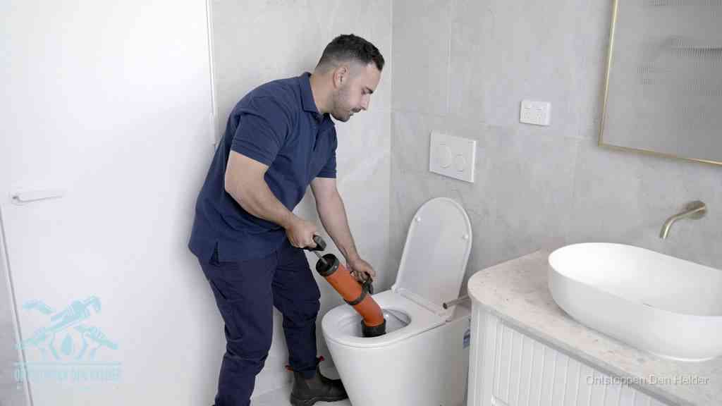 Een monteur gebruikt een handmatige perspomp (toiletontstopper) op een wandcloset tijdens het professioneel wc ontstoppen in Den Helder